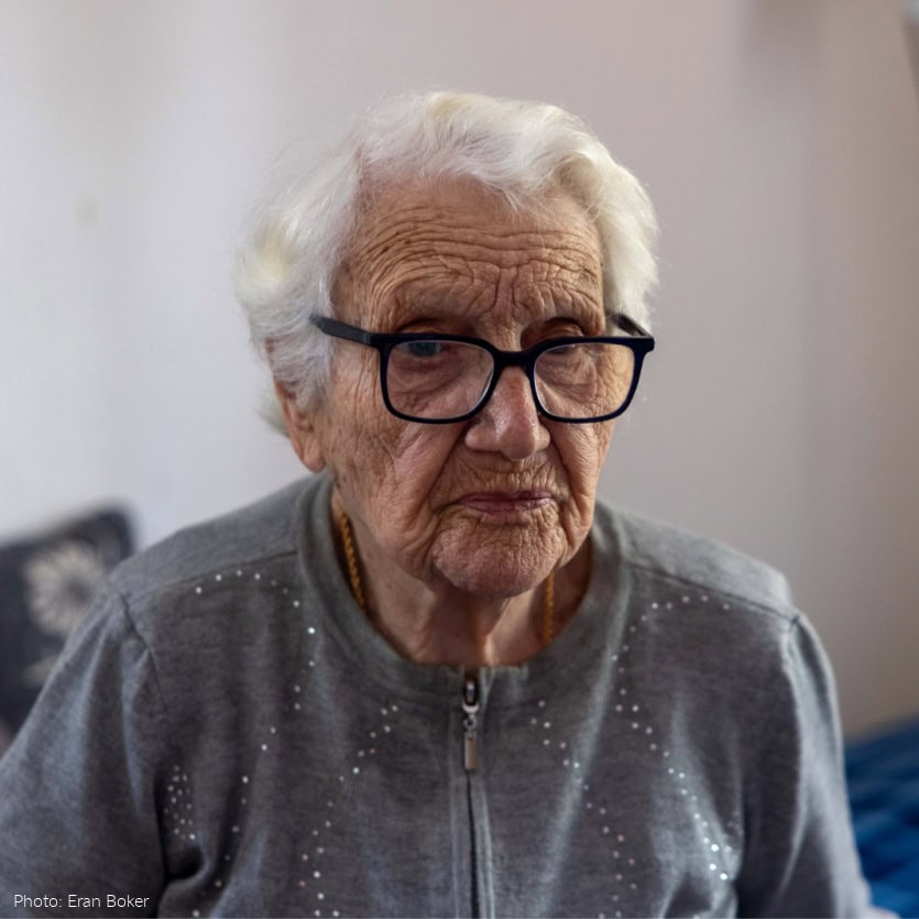 Elderly woman, gray sweater, glasses - somber expression