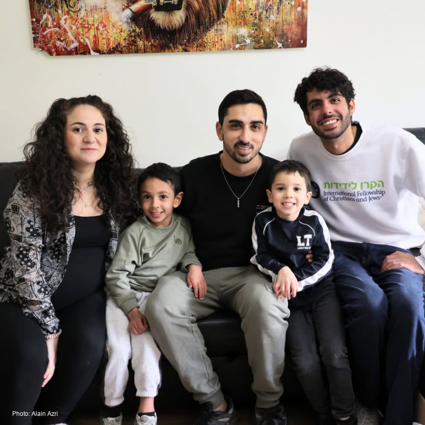 A diverse Jewish family sitting together on a sofa, smiling and enjoying quality time, symbolizing hope, unity, and support for Jewish families through IFCJ programs.
