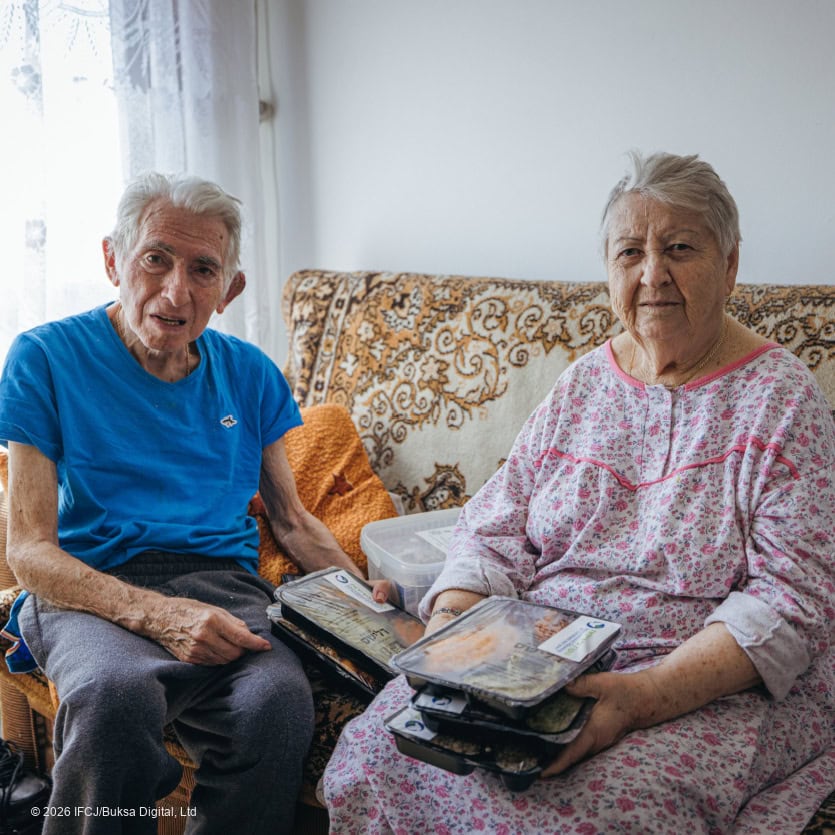 Elderly man and woman sitting on a sofa, reading books and sharing a moment of companionship, symbolizing hope and support for vulnerable seniors through IFCJ's Shine a Light initiative.