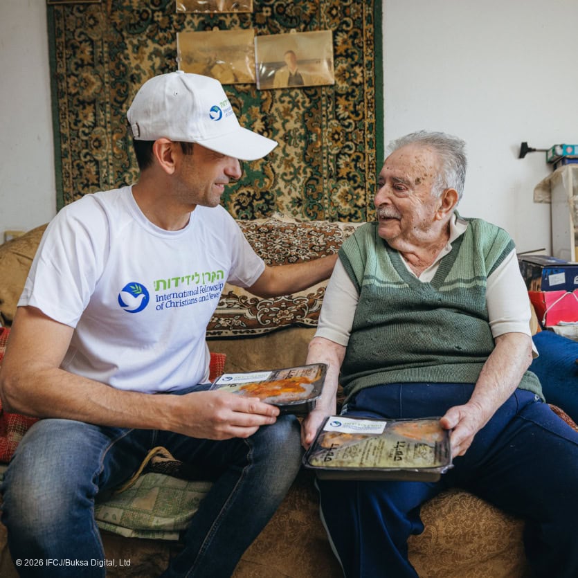 Volunteer sharing a meal with elderly woman in a cozy home setting, symbolizing compassion and support for vulnerable communities.