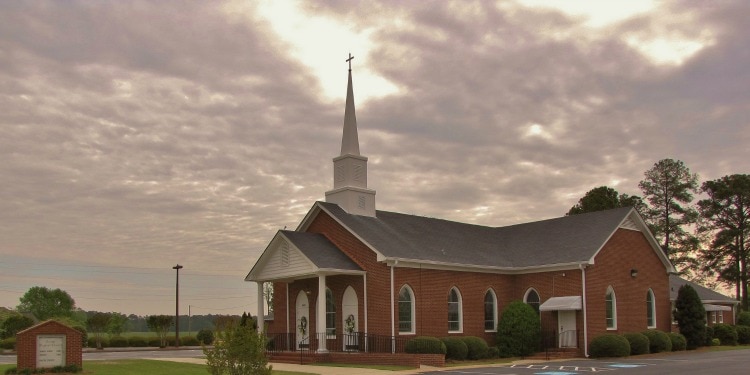 A red brick church with white accents surrounded by few trees on a cloudy day.