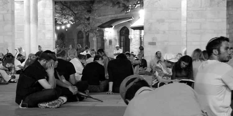 Black and image of several people sitting on the floor of a temple.