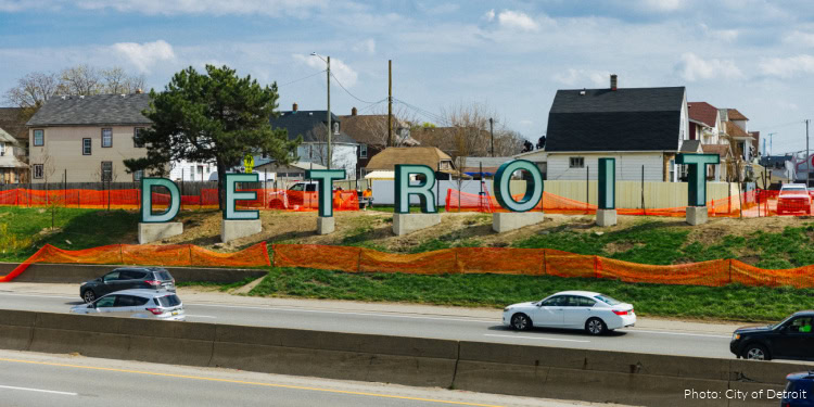 Iconic Detroit sign on a hillside with houses and trees in the background, showcasing the city's vibrant community and urban landscape.