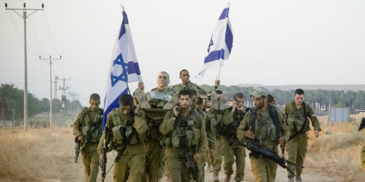 Israeli soldiers marching in a field while holding Israeli flags.