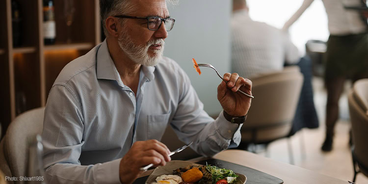 Elderly man with glasses eating a meal with a fork at a dining table, enjoying a moment of food appreciation during the IFCJ event.