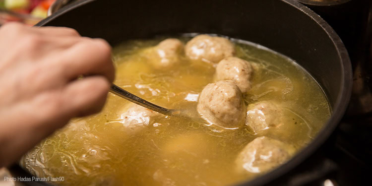 Close-up of meatballs being cooked in a simmering soup in a black pot, with a hand stirring with a spoon.
