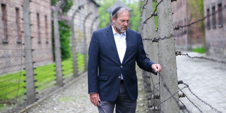 Rabbi Eckstein looking down while touching a metal and wooden fence on a trail.