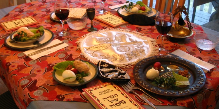 A seder table setting complete with a red table cloth and food settings for four.