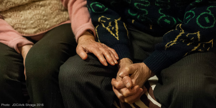 Elderly woman having her hand on an elderly man while his hands are folded.