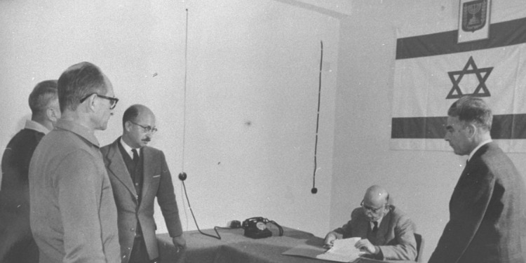 Black and white image of five men gathered around a table with an Israeli flag in the room.