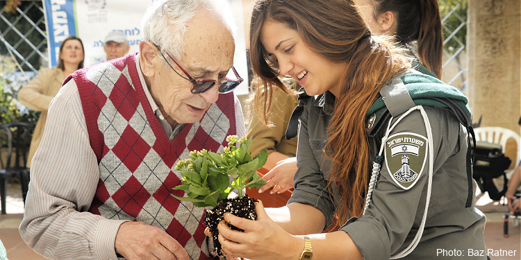 Female IDF soldier gives a plant to an elderly Jewish man. 