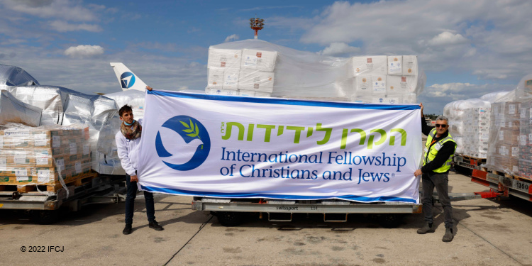 Two men holding an IFCJ banner while at an airlift station. 