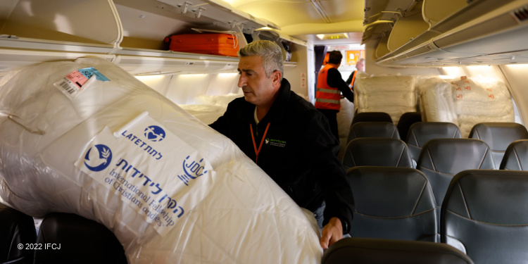 A man in an IFCJ branded sweatshirt hoisting an IFCJ blanket on a plane.