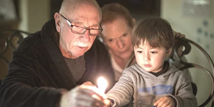 Elderly Jewish grandparents helping their grandson light Hanukkah candles.