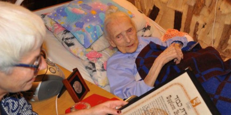 Elderly Jewish woman lying in bed while a book is read to her.