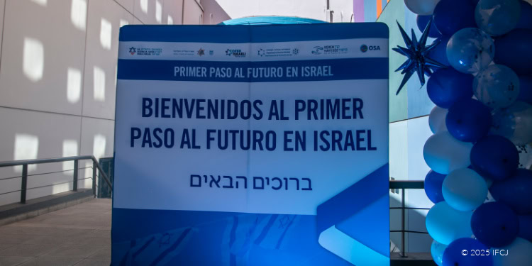 Large sign in multiple languages welcoming visitors to Israel, with blue and white decorations and balloons nearby.