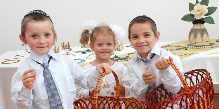 Three young children smiling at the camera while holding orange baskets.