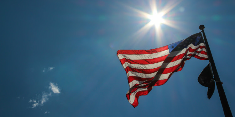 American flag waving in the sky with the sun shining behind it.