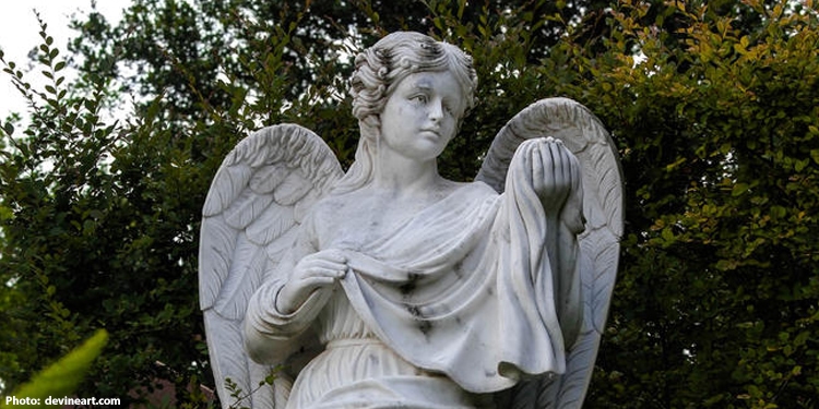 Close up image of young angelic statue with trees behind it.