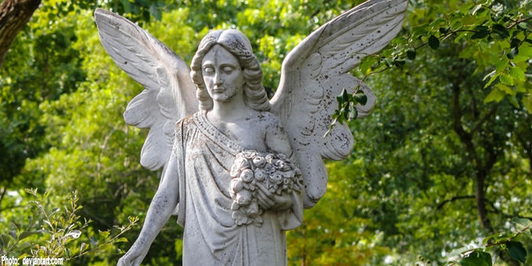 Statue of an angel holding flowers with greenery behind it.