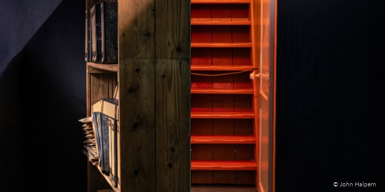 Interior view of a wooden bookshelf filled with books and documents, adjacent to a bright orange staircase, representing community support and educational initiatives.