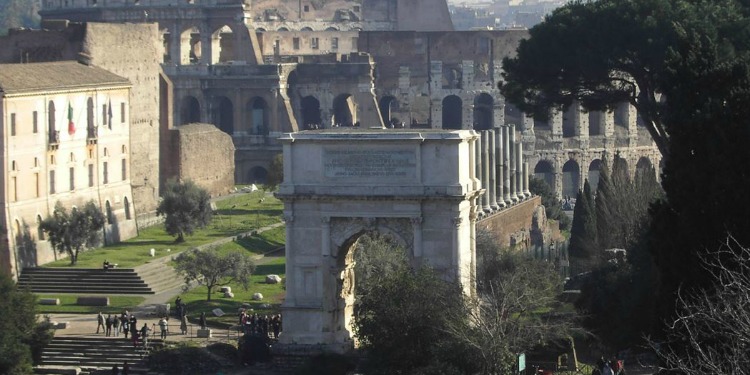 Arch of Titus with greenery and other monumental buildings around it.