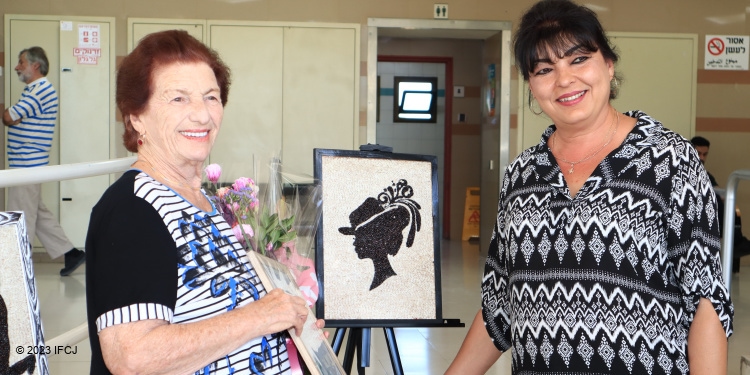Two women smiling next to a portrait of a woman at an art show.