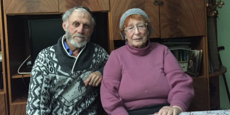 Asiya and Alexander, IFCJ recipients sitting on two chairs beside each other in their home.