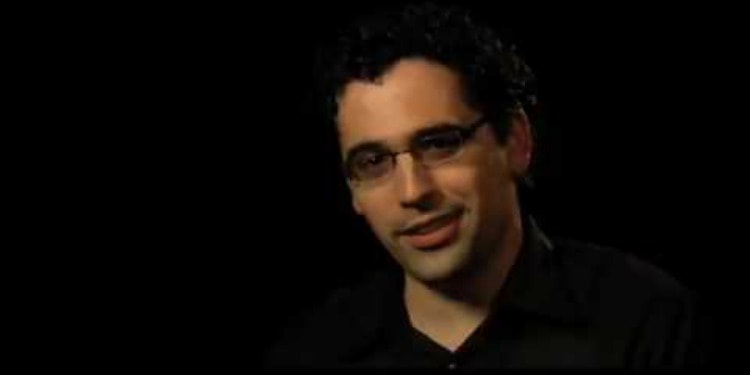 A man with glasses against a black background.