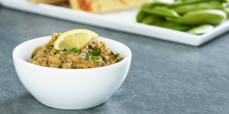 Baba ganoush in a white bowl with a lemon on top.