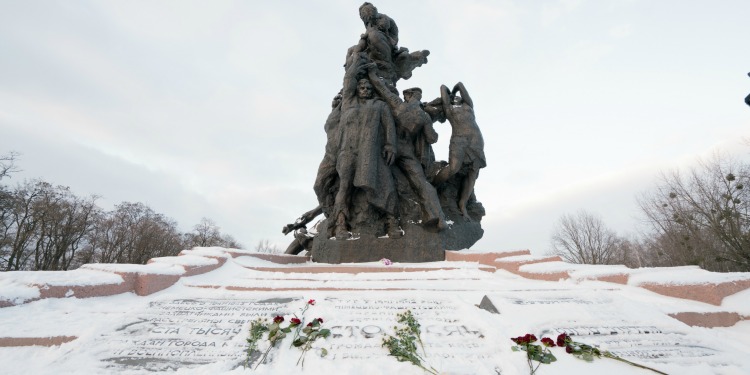A Holocaust memorial with a statue and name plate with snow and roses on top of it.