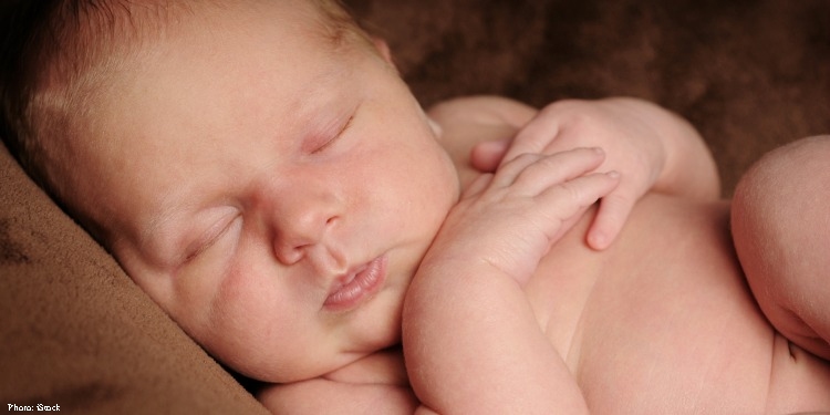 Peaceful looking newborn baby on a soft, brown blanket.