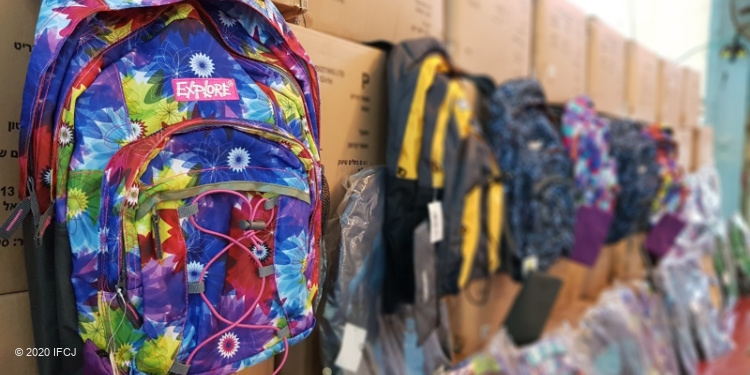 Several school backpacks for children hanging on stacks of cardboard boxes.