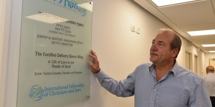 Rabbi Eckstein standing next to a dedication plaque at the maternity ward in the Barzilai Medical Center.