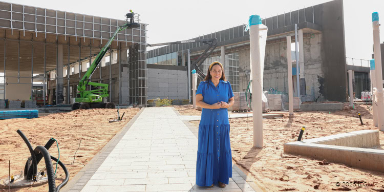 Yael Visits Beit HaLochem (Soldiers Home) - Under Construction in Ashdod, Israel - November 18, 2025 Yael Eckstein, blue dress - standing on a cement walkway in front of a building under construction