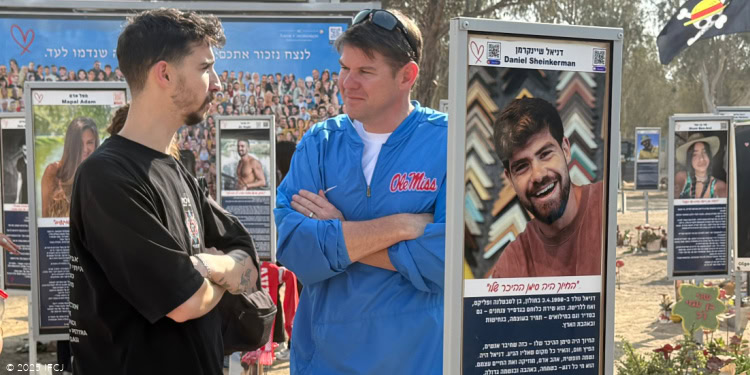 Ben Ferguson Visit to Israel - Nova Festival Massacre Site - November 5, 2025 Ben Ferguson, blue zip-up jacket with red Ole Miss logo, tan shorts - listening to Nova survivor Itay Hammer, young man, black t-shirt - signs with photos of Nova massacre victims