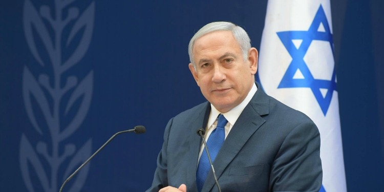 Bibi standing at a podium with the Israeli flag behind him.