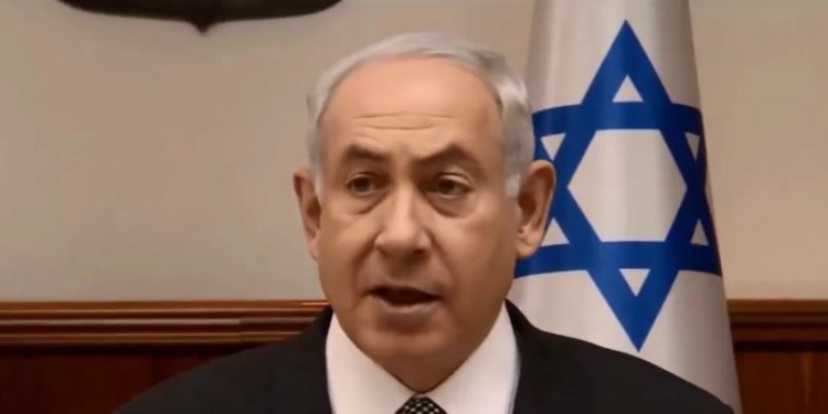 Bibi talking in front of an Israeli flag.
