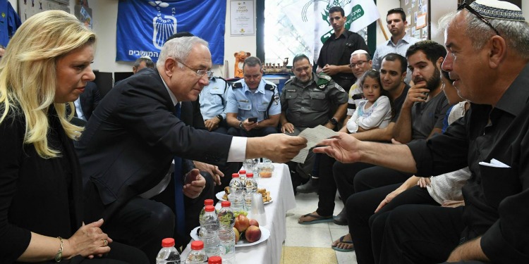 Bibi sitting with a large group of men as his wife is by his side.