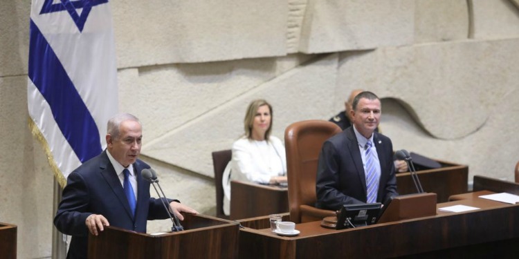Bibi giving a speech at a podium with another gentleman to his left seated at his own podium.