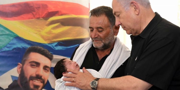 Bibi standing with the father of a young baby as they both gaze down at him.