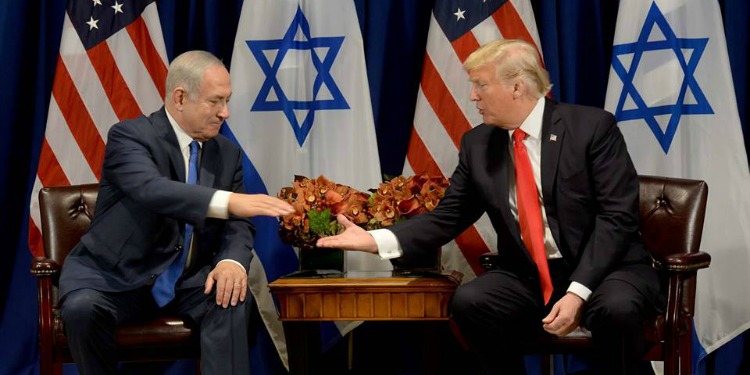 Bibi and Trump shaking hands on a stage with the American and Israeli flag.