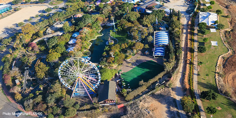 Aerial view of Luna Park featuring a Ferris wheel, roller coaster, and various rides surrounded by lush greenery and pathways.