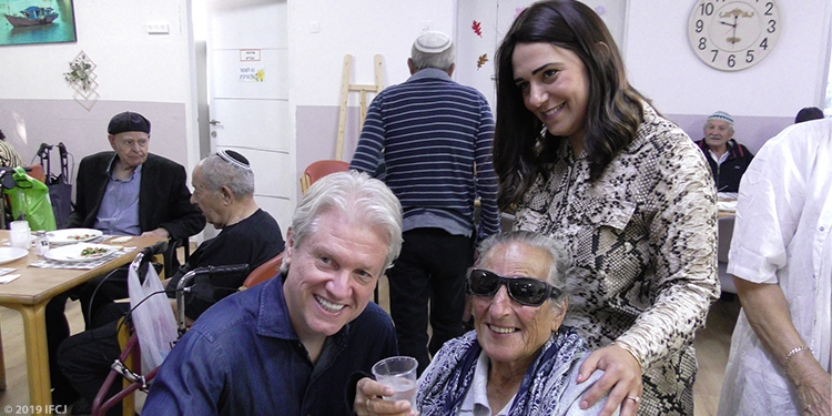 Bishop Paul Lanier smiling next to two people at an elderly club.