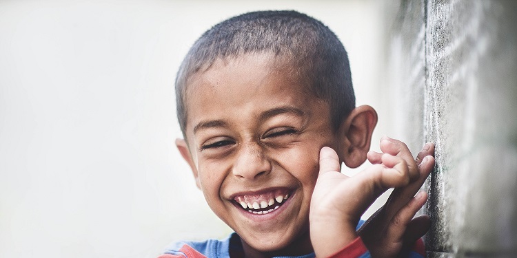 Young boy with his hands by his face laughing.