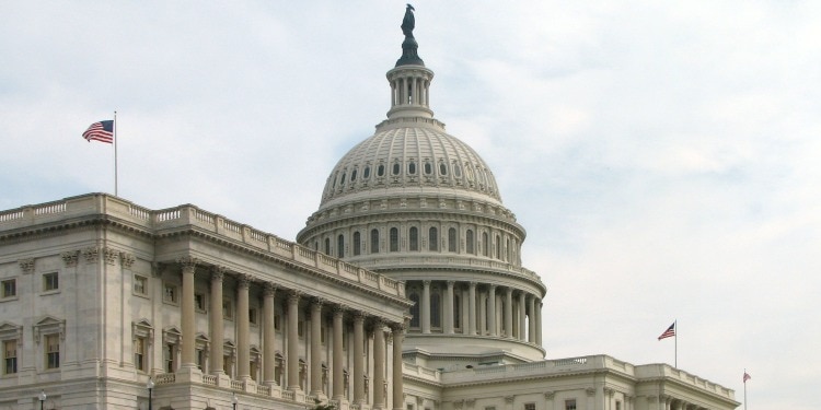 The U.S. Capitol with three American flags waving around it on a sunny day.