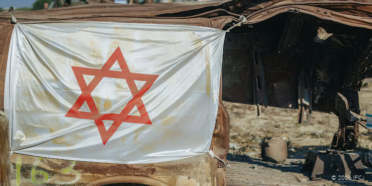 A damaged vehicle with an Israeli flag displayed, symbolizing conflict and peace efforts in Gaza, amidst a war-torn environment.