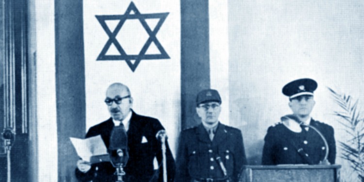 Israel's first President standing alongside two other men at a podium with a large Israeli flag behind them.