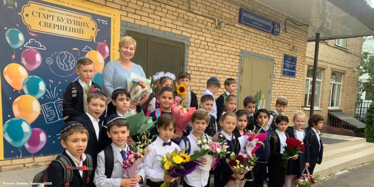 Children at Eitz Chaim School holding flowers and smiling at the camera along with their teacher.