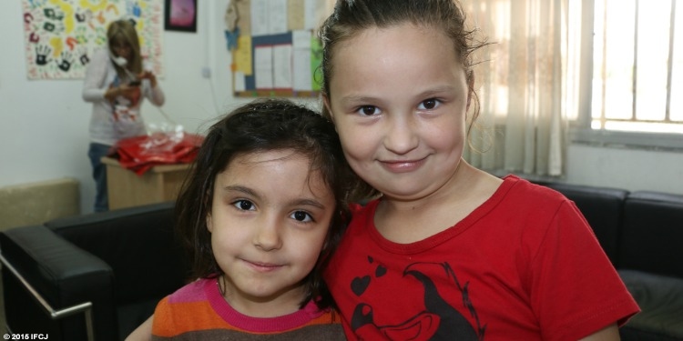 Young girl in striped shirt and young girl in red shirt smiling into camera.